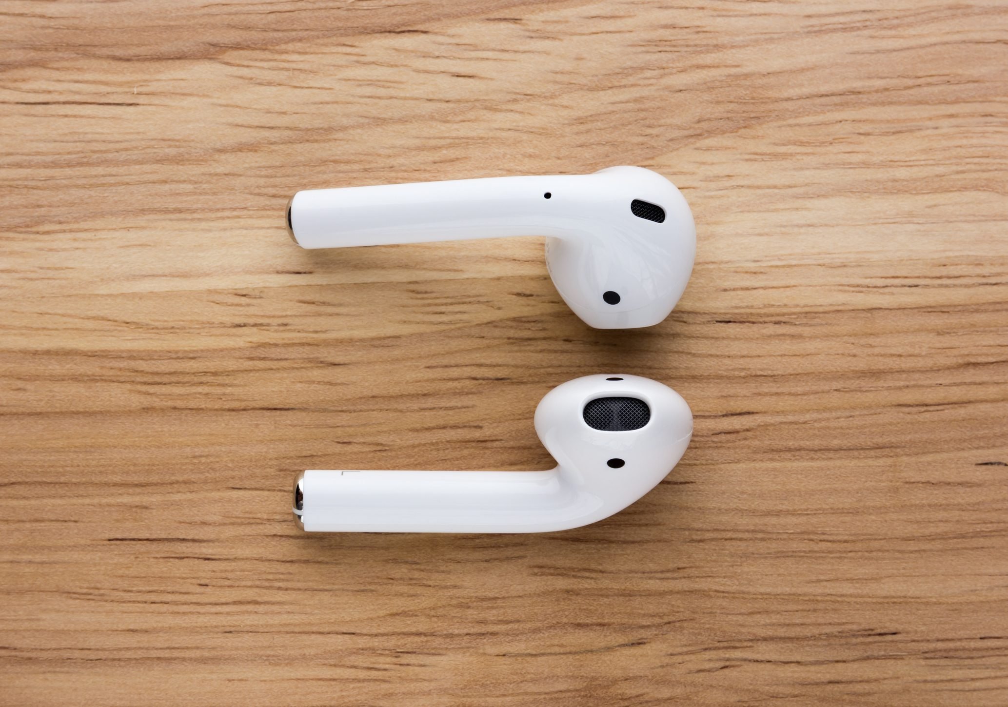 The airpods headset lies on a wooden table.