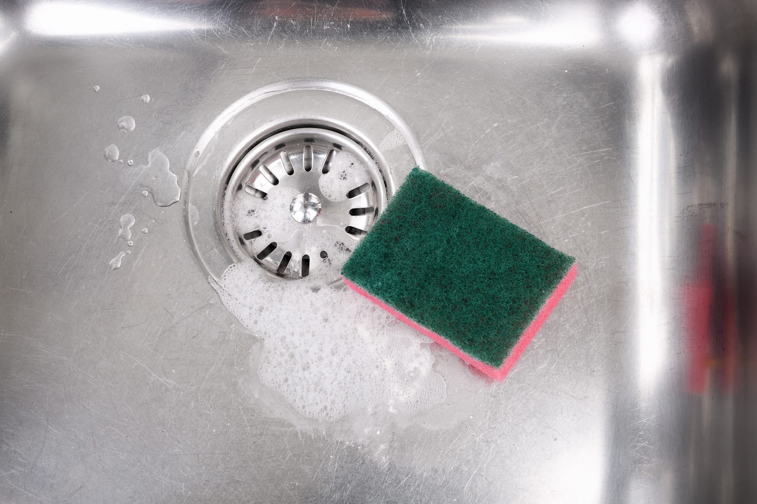 Stainless steel kitchen sink with soap suds and cleaning sponge