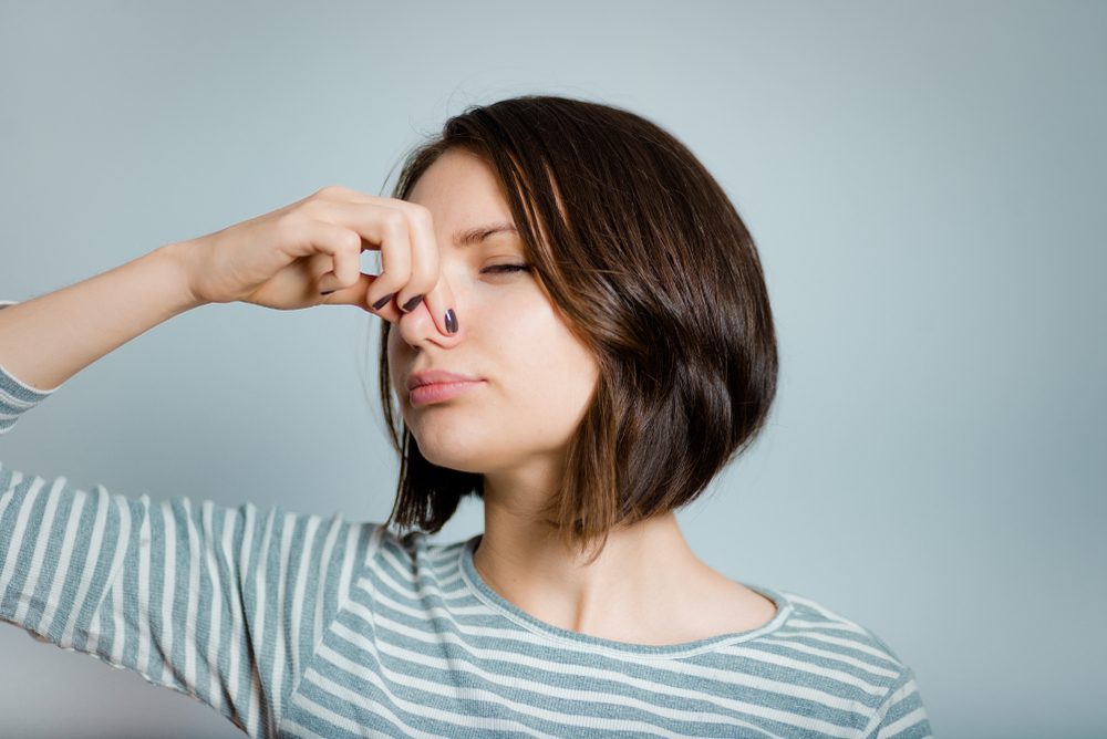 beautiful young woman closes nose because of a bad smell, isolated on background, studio photo