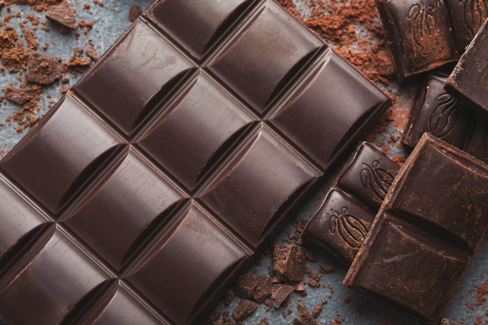 foods and drinks that cause migraines | Dark chocolate bar broken in pieces on dark background and cocoa powder closeup. Sweet wallpaper, confectionery shop advertising and cooking ingredients concept